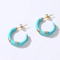 Détail de boucles d'oreilles en émail bleu en forme de C avec clous dorés sur fond blanc - Créoles en C / Bleu