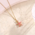 Détail du pendentif étoile de mer dorée avec émail rose sur une surface en pierre - Rose