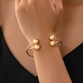 Minimalistisches goldenes Armband mit überkreuzten Linien und vier Kugeln, am Handgelenk - Gold