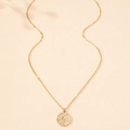 Close-up of vintage gold sun face pendant necklace on minimalist textured beige surface - Gold Sun Face Necklace