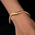 Minimalist irregular wave gold bangle with a polished finish on a model wrist - Gold
