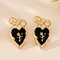 Detailed close-up of heart earrings with black enamel, gold bow, and rose embossing - Black