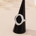Minimalist silver geometric hollow oval ring on a black display stand with warm background - Silver White