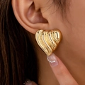 Fashionable oversized gold heart stud earrings with textured wavy surface on model - Gold Yellow