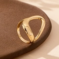 Close-up of golden irregular cutout ring on a textured dark pedestal with soft lighting - One Size / Gold Yellow