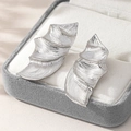 Elegant silver leaf stud earrings with brushed metal texture on a gray jewelry box - Silver White