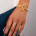 Gouden open kruis armband en bijpassende ringset gedragen door model op denim stof - Goudgeel