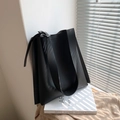 Bolso tote minimalista de cuero negro con correa ancha ajustable sobre fondo con textura - Negro