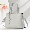 Light gray lychee pattern tote bag with pearl pendant and top handles on a desk - Gray