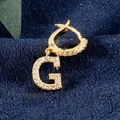 Gouden huggie oorbel met kristallen letter G-hanger op blauwe getextureerde stof - Goud G