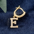 Goldene Huggie-Ohrringe mit Buchstabe E und Zirkonia-Besatz auf blauem Samthintergrund - E Gold