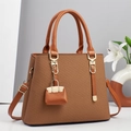 Detail of a brown woven handbag with leather handles and a mini charm hanging on the front - Khaki/Earth Yellow