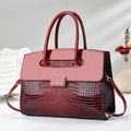 Detalle de bolso rojo de charol con grabado de cocodrilo y hebilla dorada en un soporte - Rojo