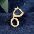 Vergoldeter Buchstabe O Huggie-Ohrring mit Zirkonia-Steinen auf blauem Samt-Hintergrund - Buchstabe O Gold