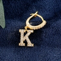 Goldener Ohrring mit Buchstaben K und Zirkonia-Besatz auf dunkelblauem Hintergrund - K-Gold