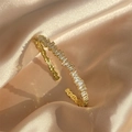 Elegant gold open bangle with geometric baguette zircons on premium silk background - Gold