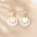 Close-up of golden drop earrings with pearlescent shell discs on a textured background - Gold