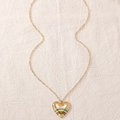 Dettaglio di una collana a cuore dorato con smalto arcobaleno su sfondo di lino beige - Oro