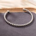 Minimalist silver twisted cuff bracelet with metal ball ends on a wooden display - Silver