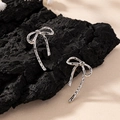 Silver bow stud earrings with hammered texture displayed on a black charcoal block - Silver