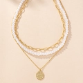 Dettaglio di una collana dorata a tre strati con catene spesse, perle e un ciondolo a moneta - Oro