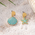 Detail of asymmetric gold earrings with blue starfish and shell on a beach sand background - Teal