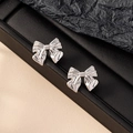 Polished silver bow knot stud earrings for women on a professional black textured display - Silver