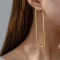 Orecchini geometrici rettangolari dorati minimalisti indossati da modella su fondo scuro - Oro