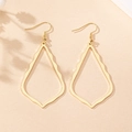 Close-up of golden hollow teardrop earrings with irregular wavy texture on neutral paper - Gold
