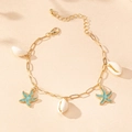 Detail of gold chain anklet featuring white shells and blue starfish on sand - Teal