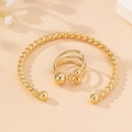 Detail van de gouden gevlochten armband en drielaagse bolletjesring op zand textuur - Armband en ring set / Goud