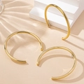 Detailopname van glanzende gouden C-vormige oorringen op een minimalistisch display - Gouden 2-delige Set