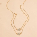 Dettaglio macro di una collana d'oro a strati con due ciondoli a cuore scintillanti - Set da 2 Pezzi Oro