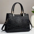 Close-up of black crocodile embossed leather handbag with gold metal hardware and strap - Black