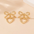 Close-up of golden bow earrings with hollow heart drop on a textured background - Gold