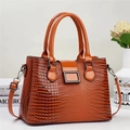 Nahaufnahme der karamellfarbenen Handtasche mit Echsenprägung und glänzendem Lack-Finish - Erdgelb