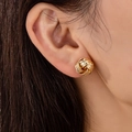 Elegant gold twisted knot stud earrings with textured finish shown on model's ear - Gold