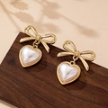 Elegante goldene Schleifenohrringe mit herzförmigen weißen Perlen auf Vintage-Holzgrund - Perlweiß