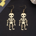 Macro detail of golden skeleton earrings with heart-shaped eyes and movable joints - Gold