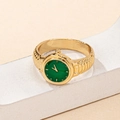 Close-up of golden watch ring with green dial and textured metal band on white stand - Green