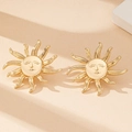 Makroaufnahme von goldenen Ohrsteckern mit Sonnengesicht auf beigem Hintergrund - Gold