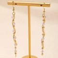 Dettaglio di orecchini lunghi a spirale dorata con perle su espositore metallico - Perla a Spirale