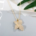 Nahaufnahme der goldenen Kleeblatt-Halskette mit Zirkonia auf grauem Hintergrund - Gold