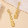 Macro shot of long irregular textured gold dangle earrings on aesthetic background - Gold