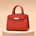 Minimalist red leather handbag with textured finish and elegant gold clasp on pedestal - Red