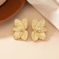 Exaggerated golden floral earrings with textured metallic finish on warm background - Gold