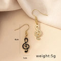Asymmetrische G-Clef Musiknoten-Ohrringe in Gold und Schwarz auf beigem Hintergrund - Violinschlüssel Stil / E93-Schlüssel (Violinschlüssel)