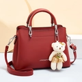 Bolso bandolera rojo con bordes ondulados, logo plateado y colgante de oso blanco - Burdeos