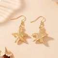 Boucles d'oreilles étoiles de mer dorées avec texture sur fond de sable fin - Doré