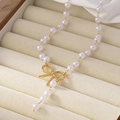 Elegante Perlenkette mit goldenem Bogenanhänger und Quaste auf beigem Samthintergrund - Weiß